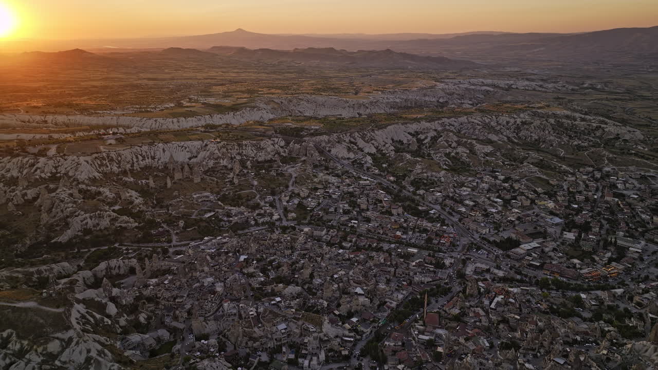 Göreme Turkey Aerial v4 birds eye view, flyover ancient village town capturing vastness of cappadocia surreal landscape with glowing sun setting in the horizon - Shot with Mavic 3 Cine - July 2022