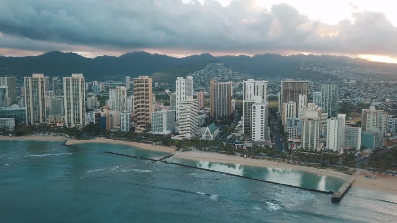 Panning aerial drone slowly flying over a colorful Honolulu Skyline while Sunset in Oahu, Hawaii with Waikiki Beach as a special point of interest.