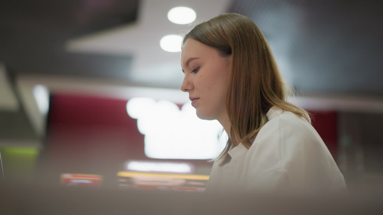 Side profile of young woman deeply focused on work in a modern indoor setting with abstract blurred background lighting, showcasing concentration
