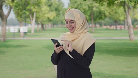 happy muslim woman using phone in park