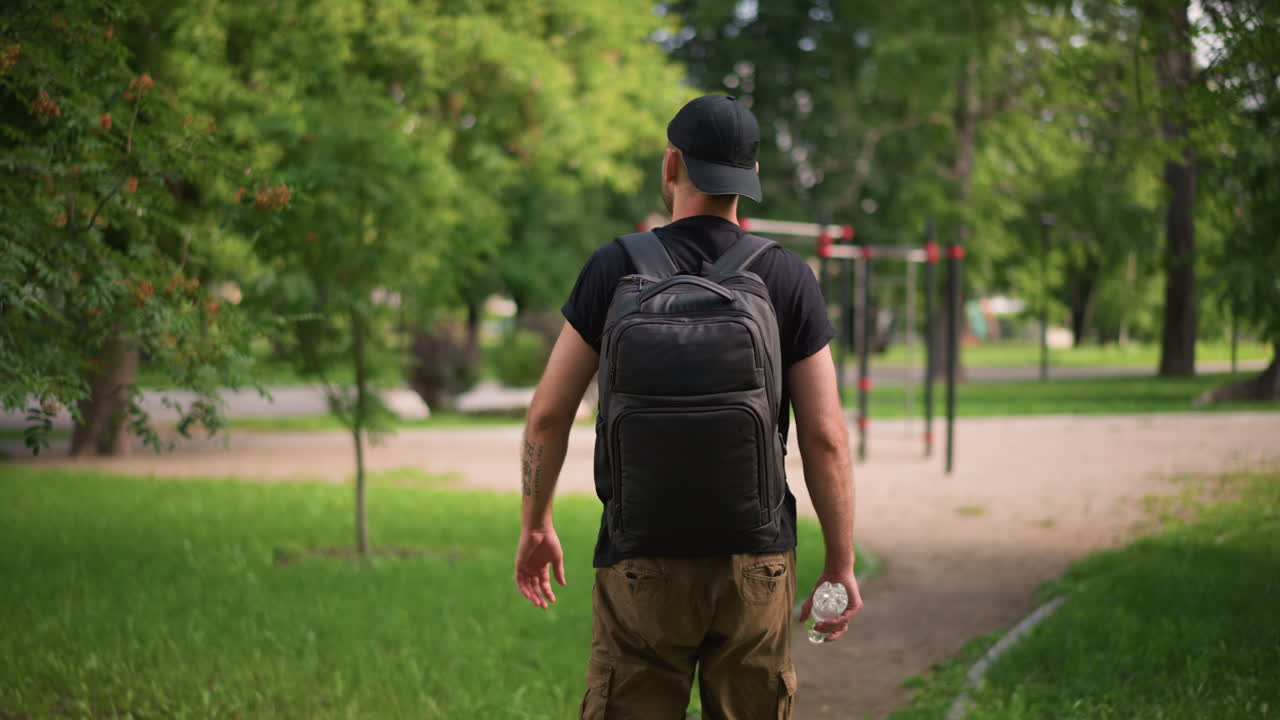 Casual Man Walking With Hydration Gear, Fitness Enthusiast Strolling Outdoors With Water And Backpack, Healthconscious Individual Enjoying Light Walk Amid Green Trees While Staying Hydrated