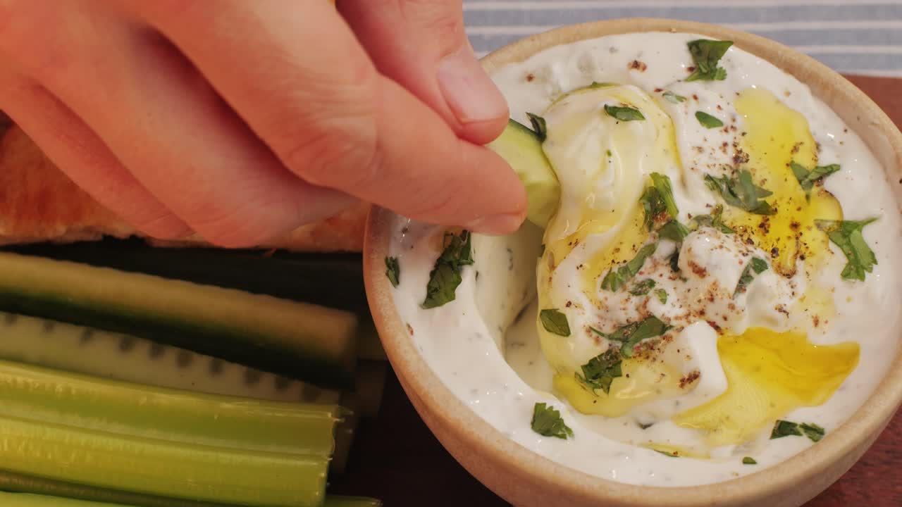 Hand dipping cucumber and celery sticks in Yogurt Dip with Pitas