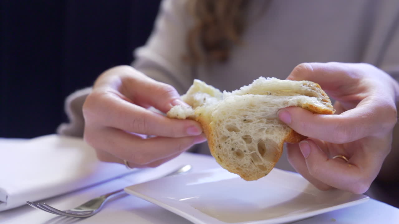 manos de mujer rasgando pan en una mesa de restaurante