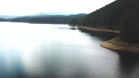 Un-Dron-Delantero-Disparó-Ligeramente-Sobre-Un-Lago-Que-Se-Elevaba-Gradualmente-Con-Un-Bosque-Al-Fondo