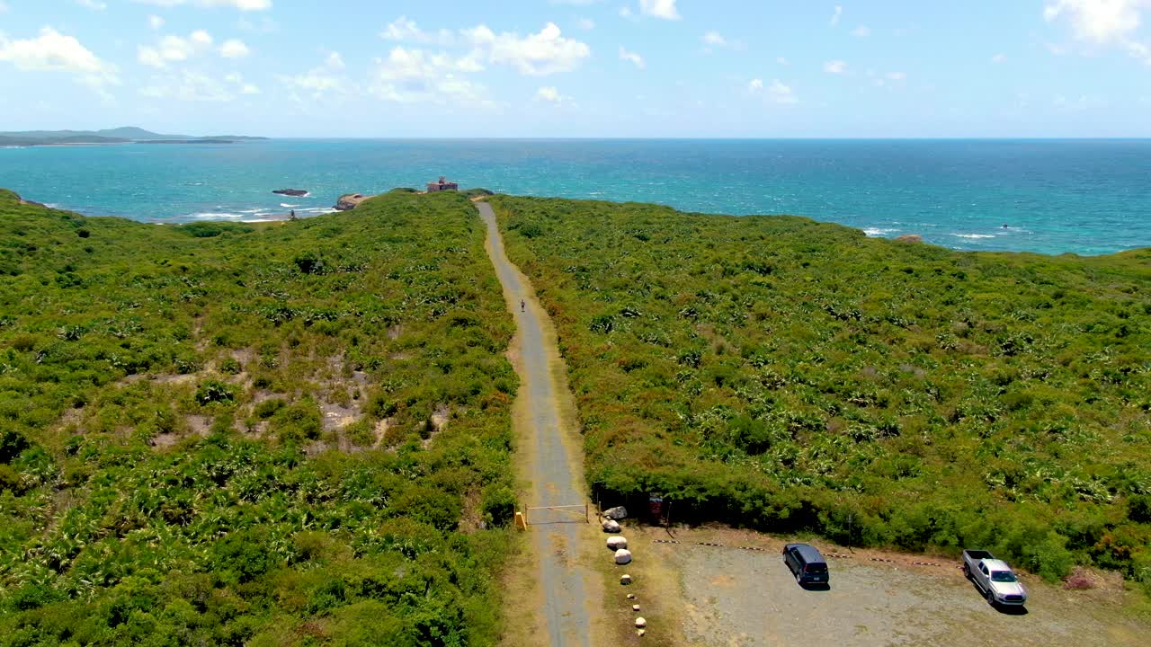 Aerial over a trail through shrubs to Puerto Ferro Lighthouse, with ocean and sky