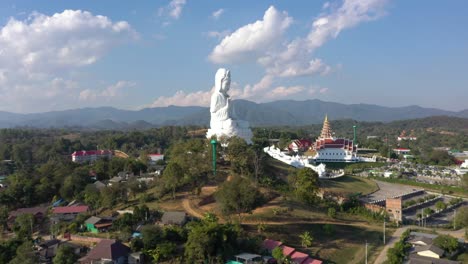 increíble dron aéreo volando hacia wat huay pla kang gigante estatua blanca grande y templo pagoda con montañas y espacio terrestre en chiang rai, tailandia