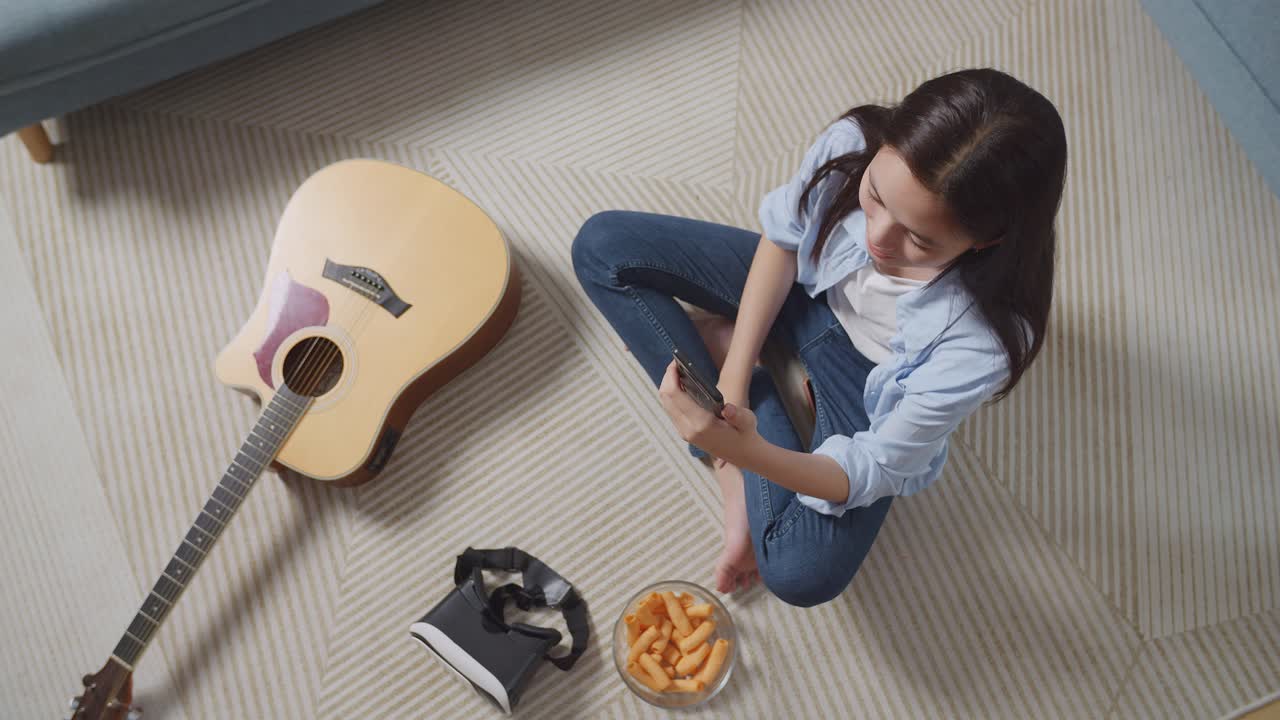 집에서 바닥에 카에 앉아서 스마트폰으로 비디오 통화를 하는 아시아 십대 소녀의  뷰. 손을 흔들고, 미소 짓고, 말하고