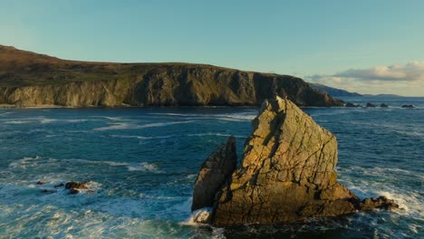 drone flying over a large rock in the ocean towards the wild atlantic way in ireland