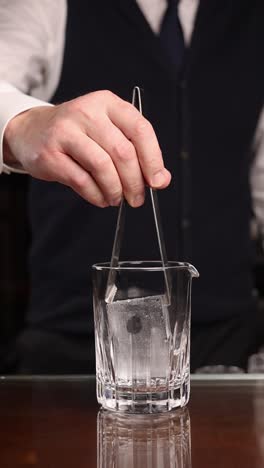bartender using ice tongs to add ice to a cocktail glass