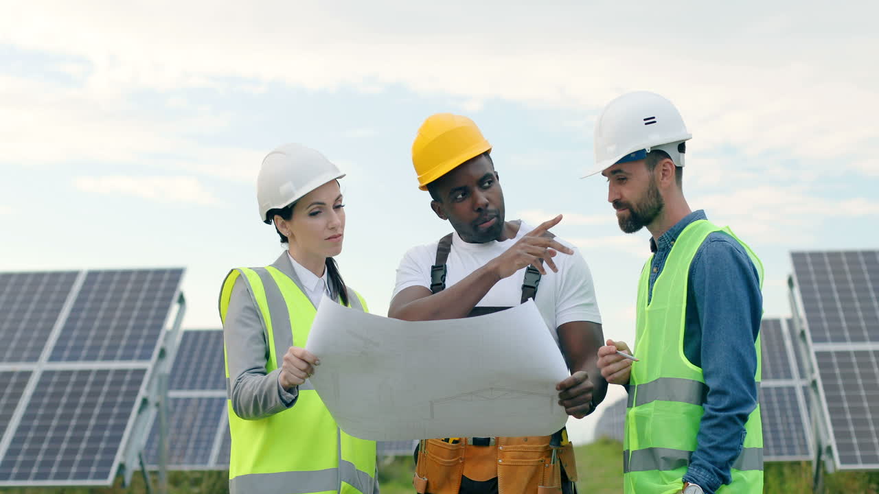 Three multiethnics farm solar engineers talking while looking at blueprint on solar plantation