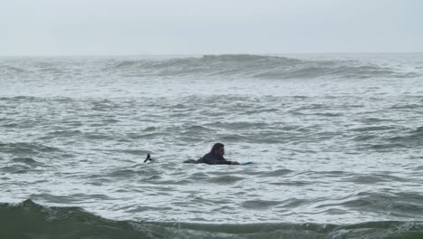 Hombre-Deportivo-En-Traje-De-Neopreno-Con-Pierna-Artificial-Acostado-En-La-Tabla-De-Surf-Y-Nadando-En-El-Océano-1