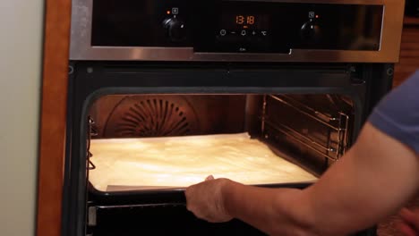 opening oven and putting in a baking tray with a shallow sponge cake