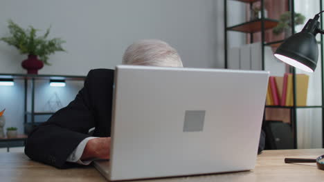 Senior-mature-older-business-man-hiding-behind-laptop-computer,-making-funny-face,-fooling-around