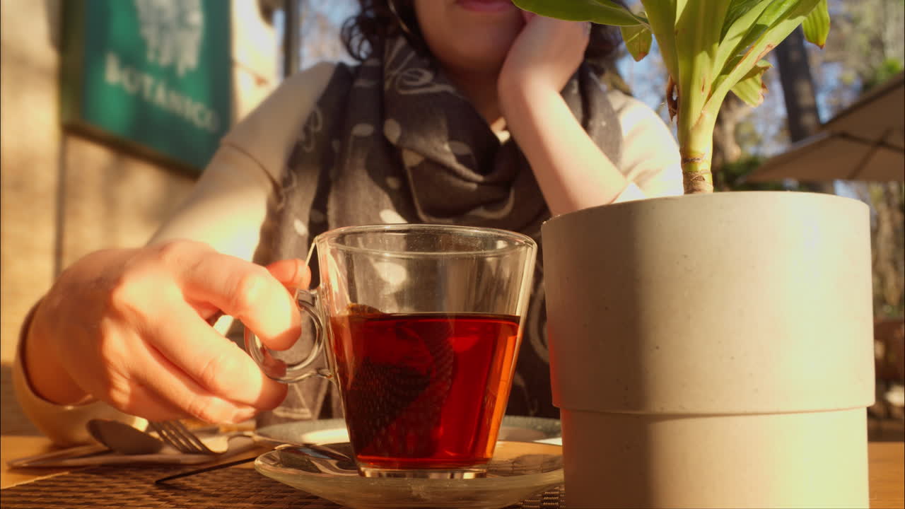 Mujer disfrutando de una taza de té caliente en una cafetería al aire libre.