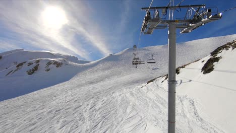 View-from-a-skilift-over-a-ski-slope-in-a-snowy-mountain-landscape,-on-a-sunny-day