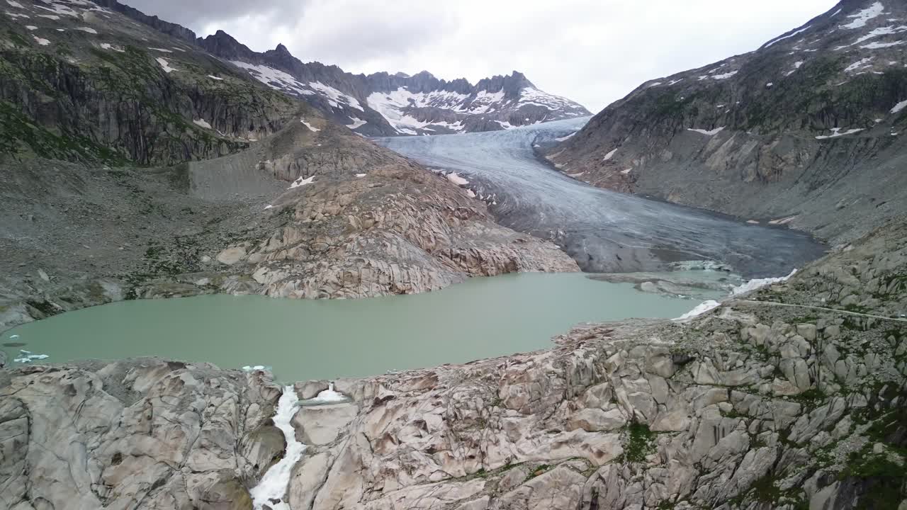 Rhone Glacier at Furka Pass in Switzerland during cloudy day with lake shot from a drone