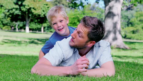 Father-smiling-while-lying-on-the-grass-before-his-son-peeks-his-head-out-from-behind-him