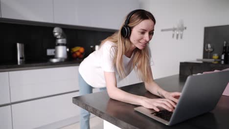 Frau,-Die-Zeit-Mit-Laptop-Verbringt,-Der-Kopfhörer-In-Der-Küche-Trägt