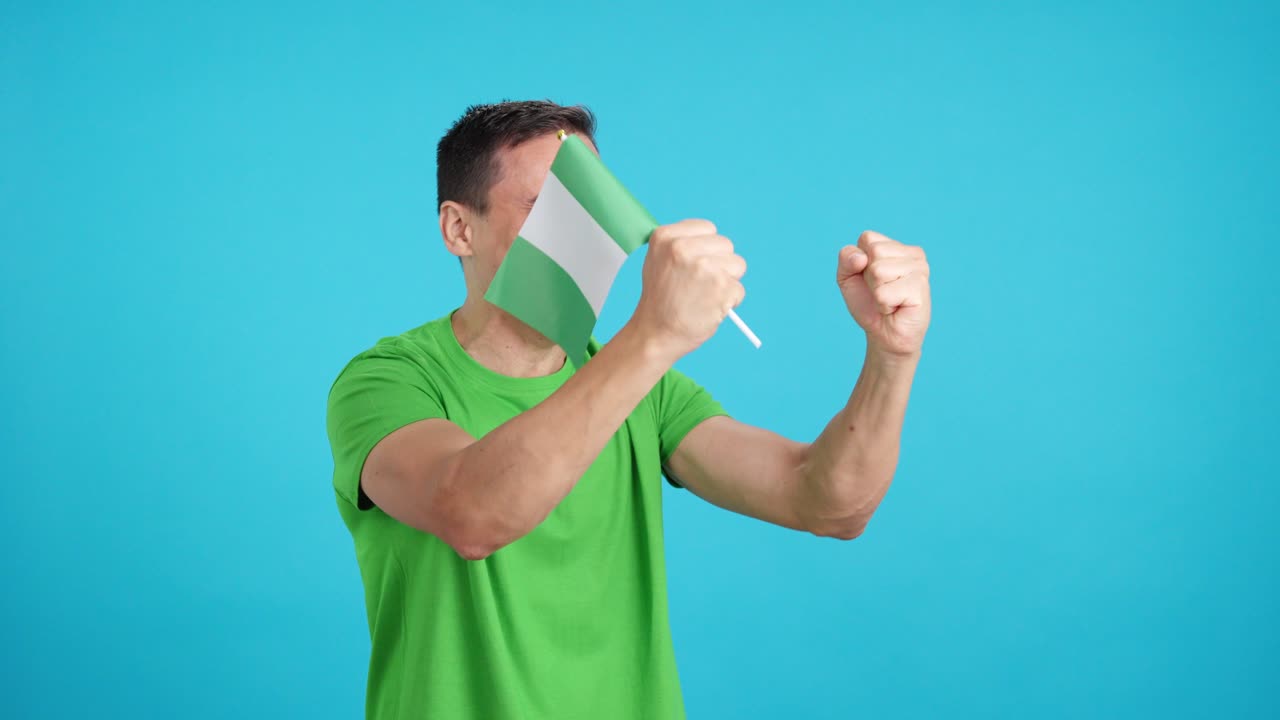 Man cheering for Nigeria waving a national flag looking away