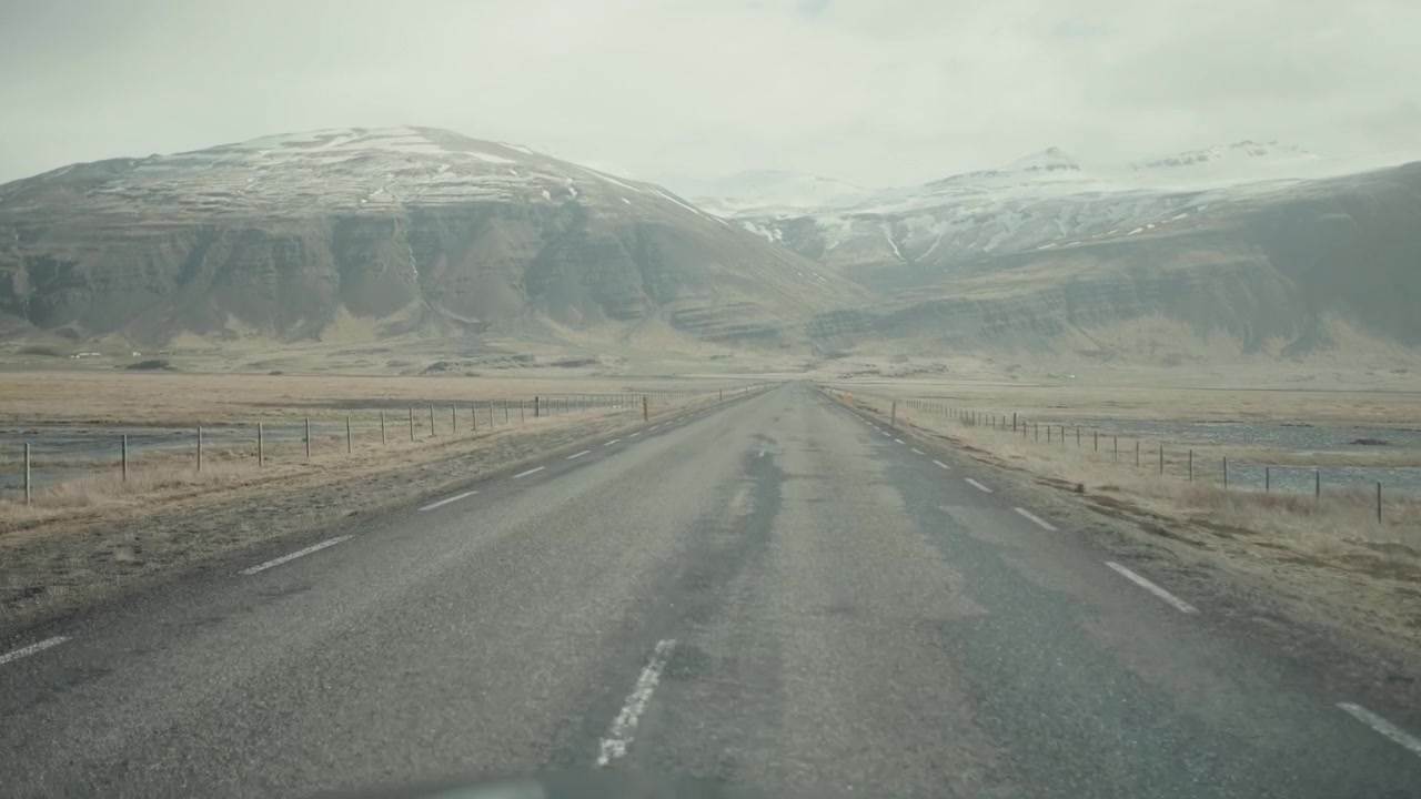 Driving on a Long Road Through a Vast Icelandic Landscape with Snow-Capped Mountains