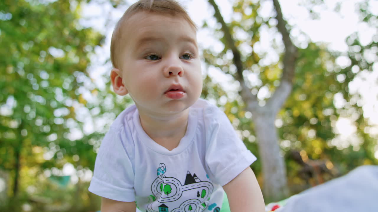 Curious Caucasian kid in t-shirt crawls by the ground. Baby boy looking around and touching camera with interest. Close up. Low angle view.