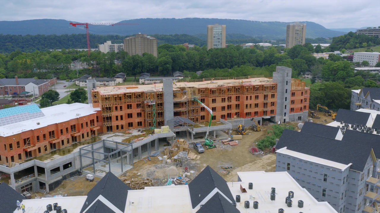 Drone shot of a brick apartment building under construction in Chattanooga, Tennessee, with a tower crane and mountain ridge in the distance.