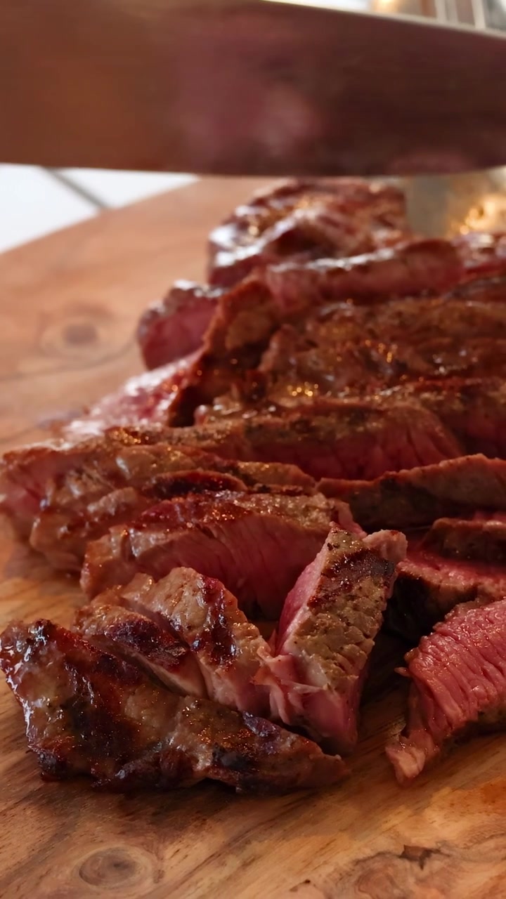 Uno chef affetta una bistecca di manzo cotta a puntino, accompagnata da verdure fresche ed erbe aromatiche, in una cucina luminosa.