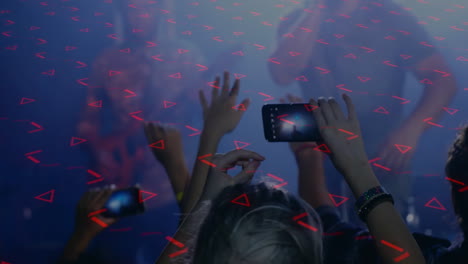 crowd raising smartphones while capturing live music show, with red triangular lights sweeping haze