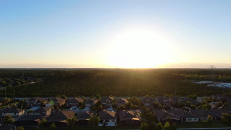 Pan-Con-Un-Destello-De-Lente-A-Través-De-Casas-Y-Una-Granja-De-árboles-De-Naranja-Durante-Una-Hermosa-Puesta-De-Sol