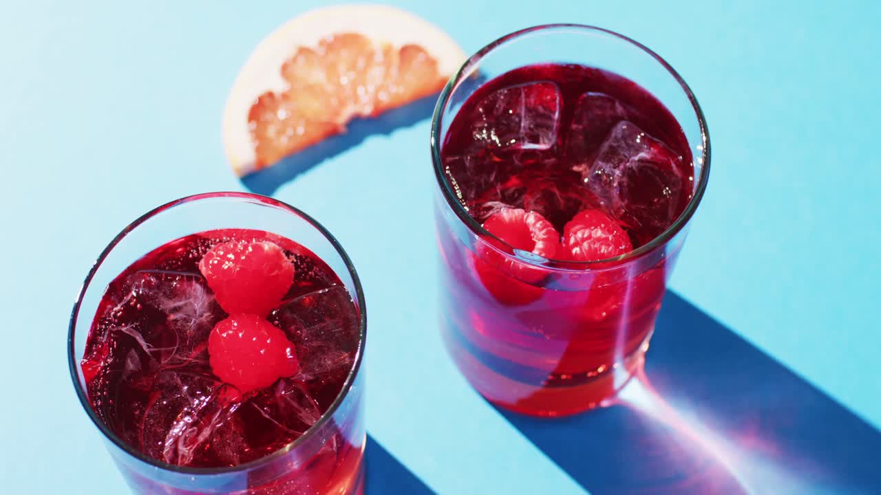 Close up of drinks with raspberries and grapefruit over blue background