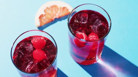 close up of drinks with raspberries and grapefruit over blue background