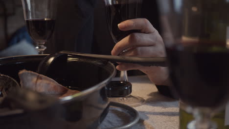 Hands-of-woman-drinking-red-wine-and-nibbling-food-from-pot-at-dinner-table