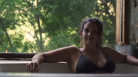 young attractive female having a fancy bath in a jacuzzi with big green nature window looking to camera smile able to slow motion 60fps