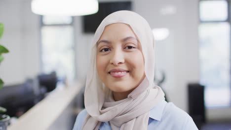 Portrait-of-happy-biracial-businesswoman-wearing-hijab-in-office,-slow-motion