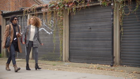 Stylish-Young-Couple-Walking-Past-Garages-On-City-Street