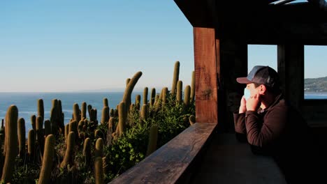 Hombre-Mirando-El-Atardecer-Con-Mascarilla-Y-Quitándose-Protector-Solar-Para-Respirar-Aire-Fresco-Covid-19-Pandemia-Para-Estar-Saludable-Desde-El-Marco-De-Una-Venta-En-Un-Mirador-De-Pichilemu-Punta-De-Lobos-Chile