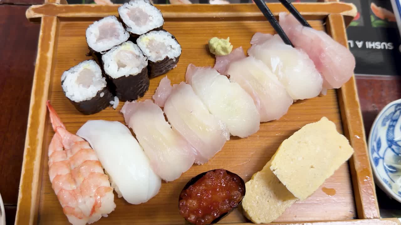 Ripresa dall'alto di sushi fresco, sashimi e roll maki presi con le bacchette.