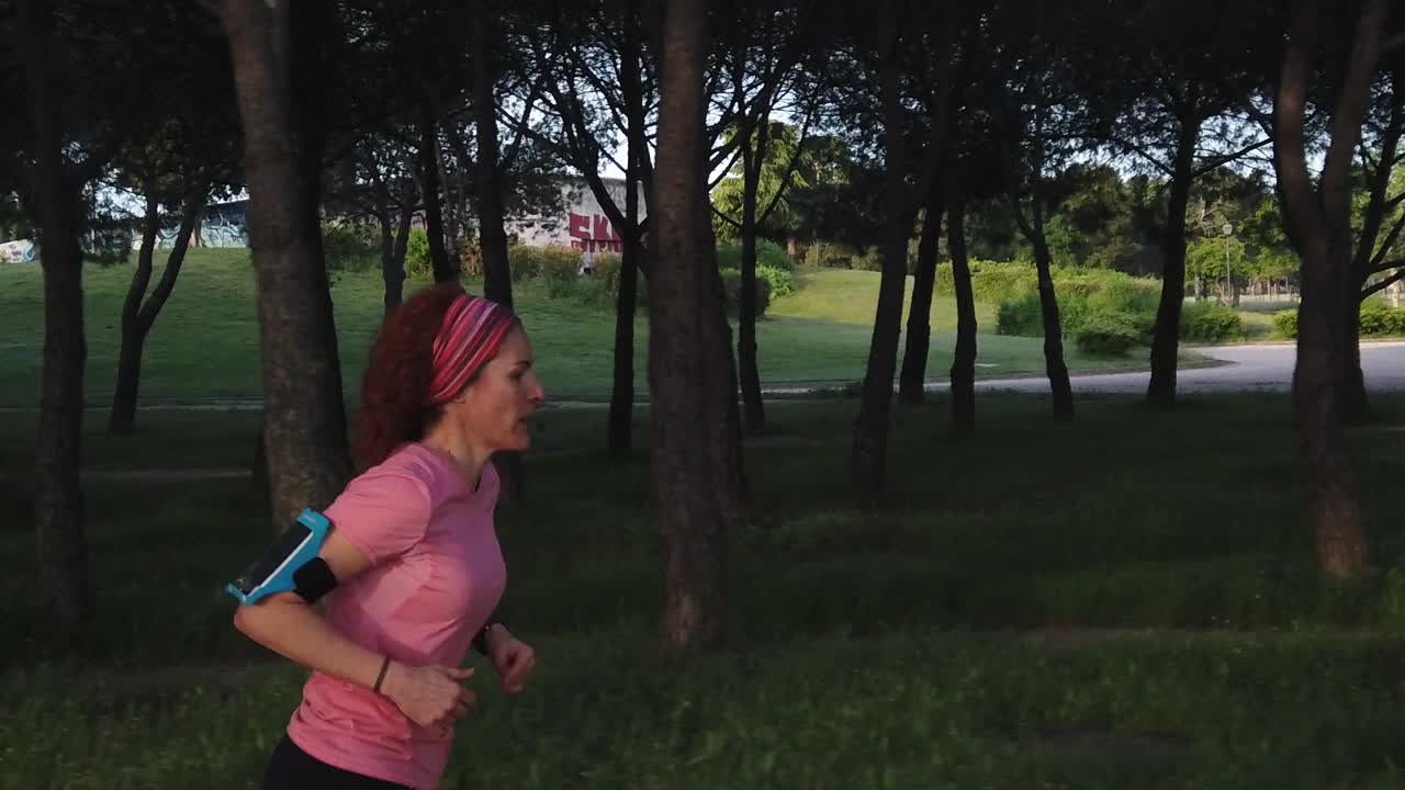 A lateral follow of a running woman. She´s running between trees in a park