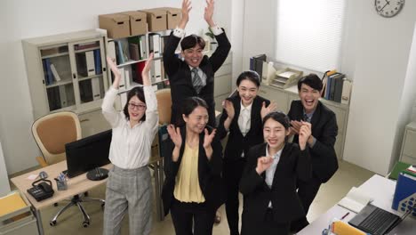 slow motion with view from above happy asian company team looking at camera and celebrating with high five and applauding for teamwork success in a modern office