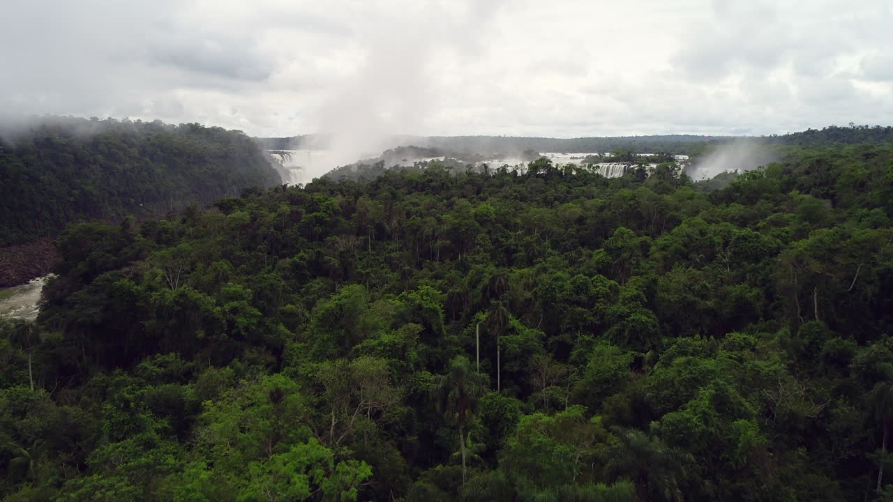 Drone ascend above tropical jungle to low lying clouds and mist water spraying from Iguazu waterfall