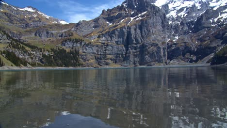 low-angle-shot-of-a-lake,-the-high-alp-mountains-and-woods-surround-it