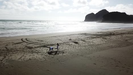 toma aérea de amantes dibujando oídos y nombres en la playa