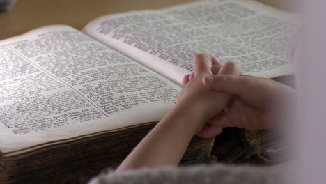 clasped hands of child praying on scripture book