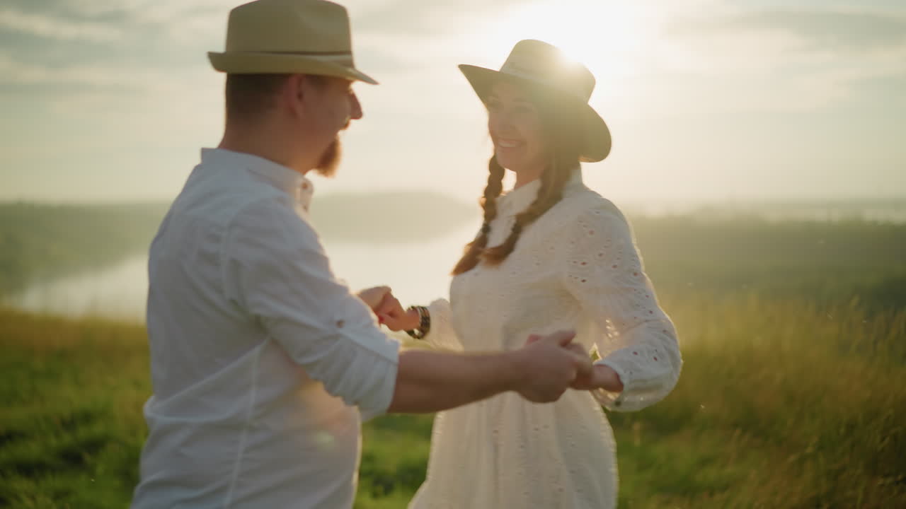 두 연인이 빛이 비치는 에서 우아하게 춤을 추는 클로즈업, 둘 다 색 옷을 입고 모자를 쓰고, 따뜻한 황금빛은 그들이 친밀한 순간을 공유하는 동안 만적인 분위기를 향상시니다.