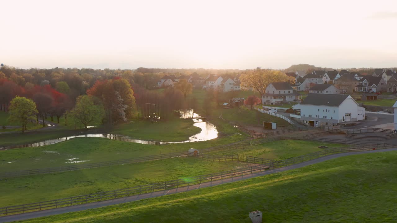 Aerial approach of farmland and horse pasture with fence, meadow and stream