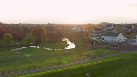 Aerial-approach-of-farmland-and-horse-pasture-with-fence,-meadow-and-stream