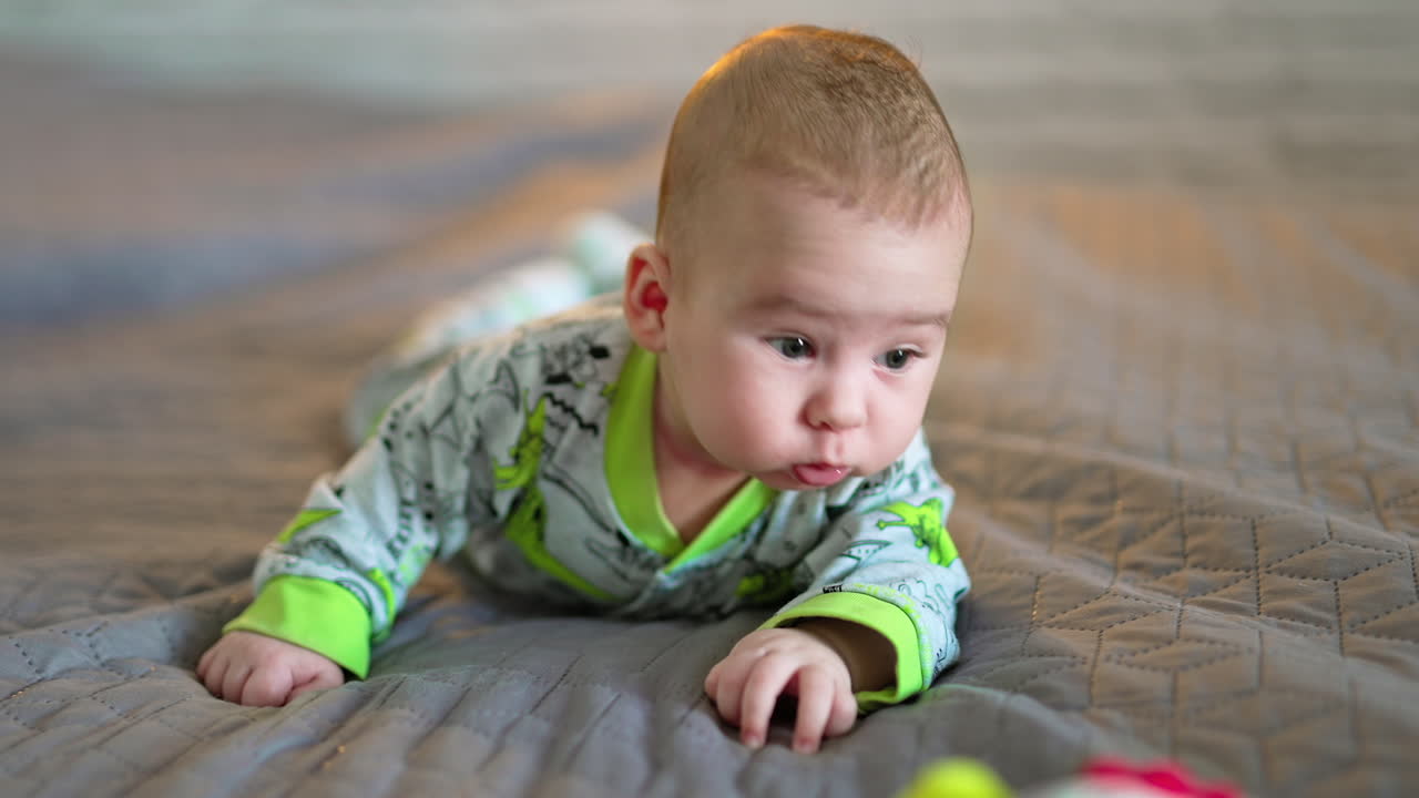 Sweet funny toddler lies on grey plaid and wants to get to the toy. Healthy Caucasian child on the blurred background.