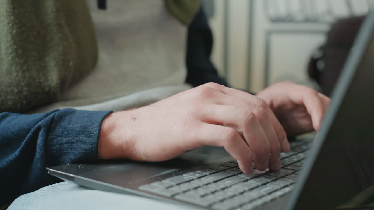 Closeup hands typing laptop keyboard freelancer in cozy apartment wearing sweater, concentrated workflow, natural light, notebook beside laptop, soft film grain, deliberate keystrokes, productive