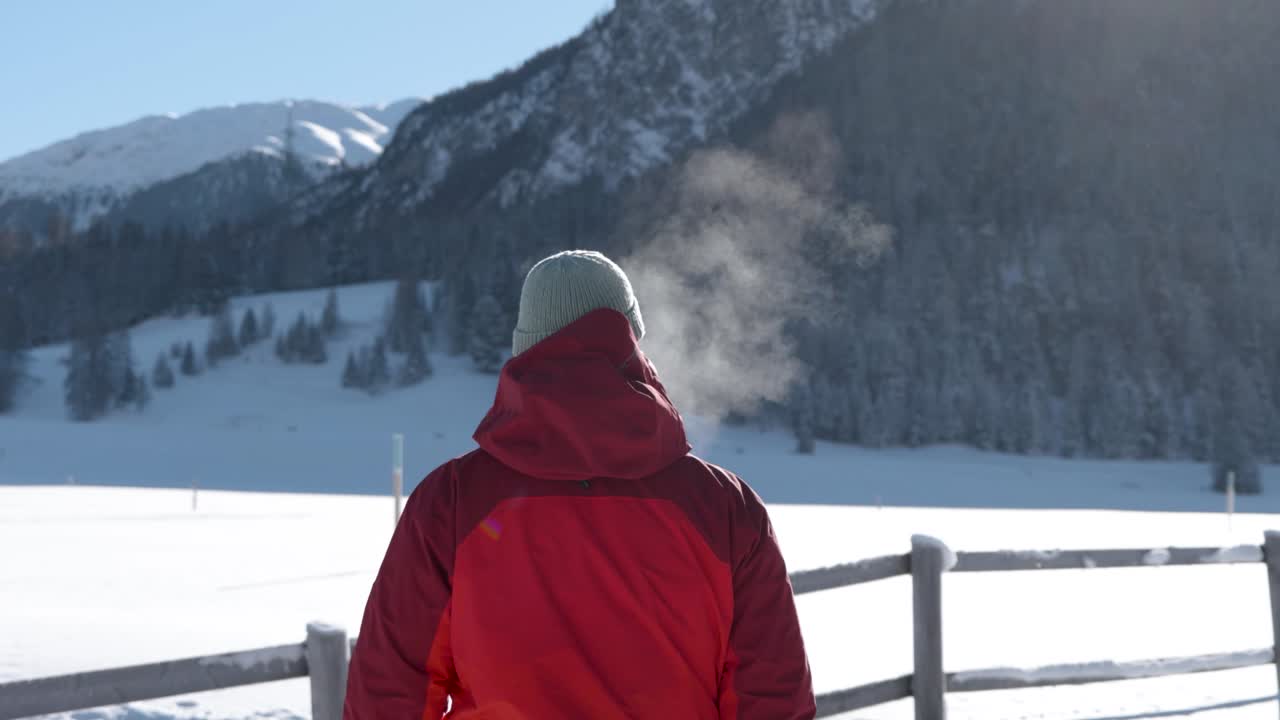 vista trasera de un hombre caucásico caminando a través de un paisaje cubierto de nieve y exhalando fuertemente en un día soleado
