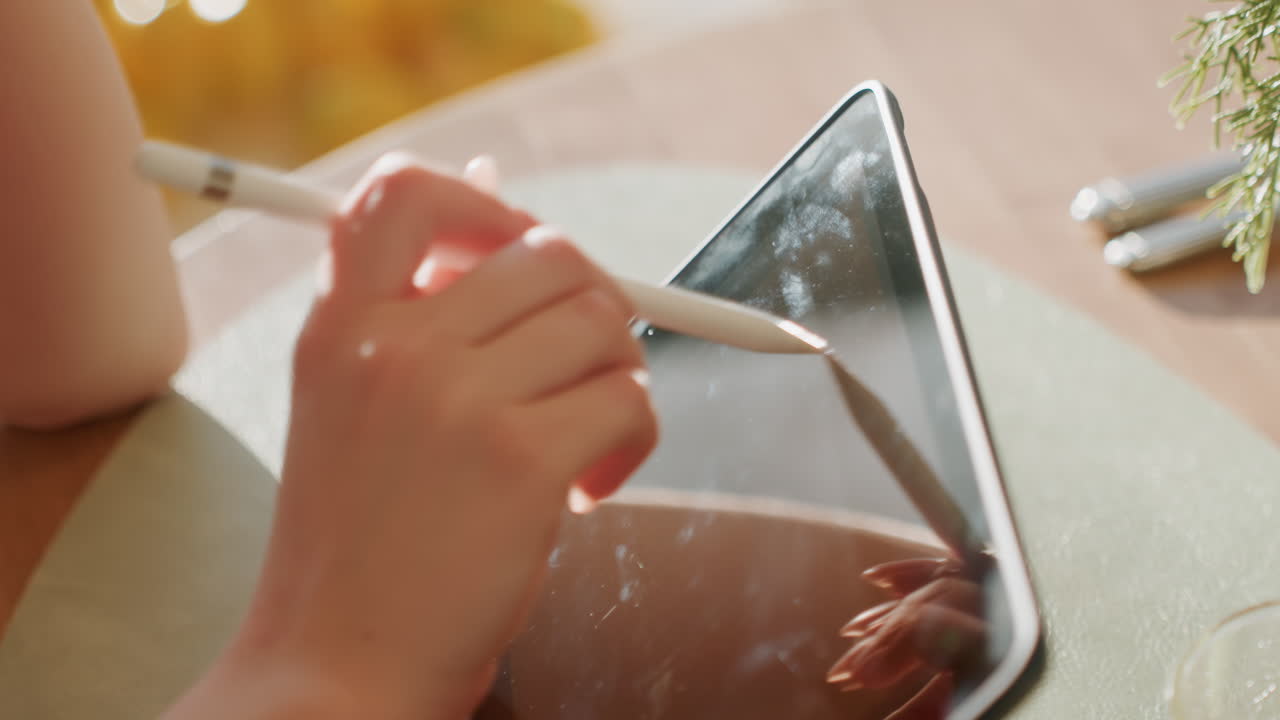 Mão em close-up tocando a borda do tablet com caneta stylus, selecionando o menu do aplicativo, entrada precisa e movimento do cursor. Copo de bebida em tampo de mesa de madeira, bokeh ambiente e uma atmosfera de produtividade relaxada em um cenário urbano casual.